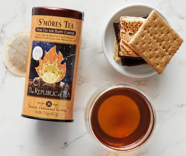 Canister of S'mores Tea with chocolate, graham crackers, and a cupful of tea, promoting a low-caffeine, affluent chocolatey beverage flavor
