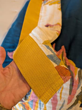 Close-up of a idiosyncratic   holding the sleeve of a patterned garment with intricate stitch detailing, highlighting cloth  texture and design