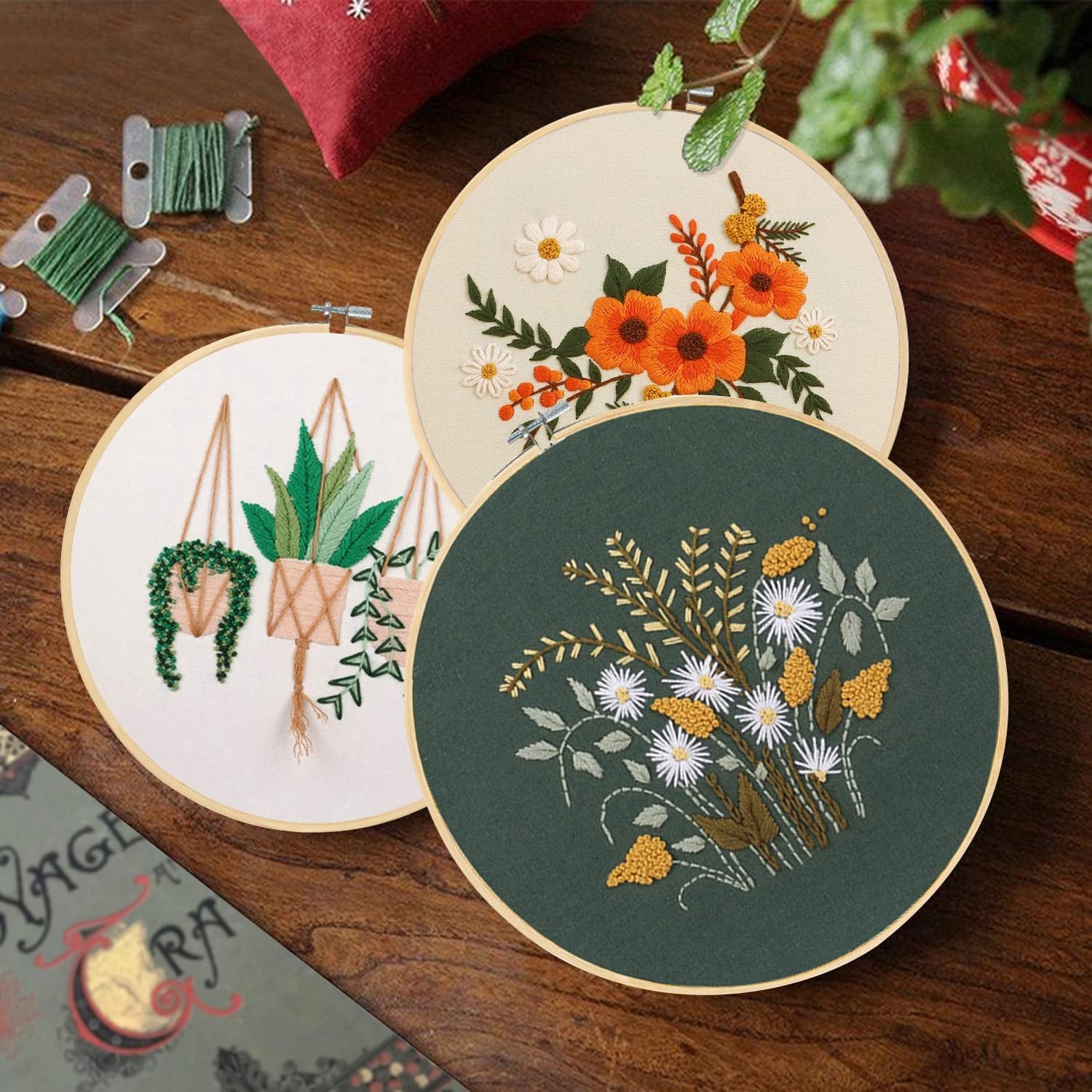 three embroidery hoops, one with orange flowers, one with wild flowers, and one with houseplants