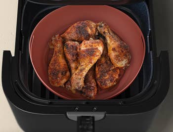 Air fryer basket with cooked, seasoned chicken drumsticks arranged on a plate inside