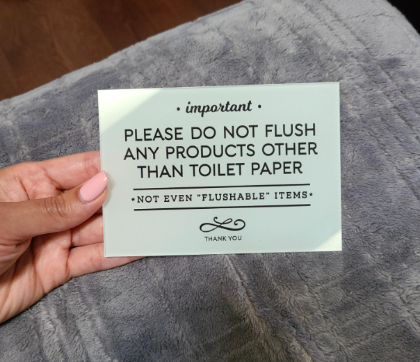 Reviewer holding small sign that says please do not flush any products other than toilet paper