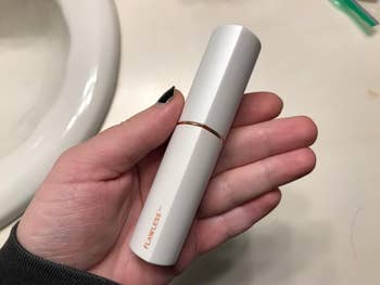 reviewer holding the white hair remover, which looks like a large tube of lip gloss