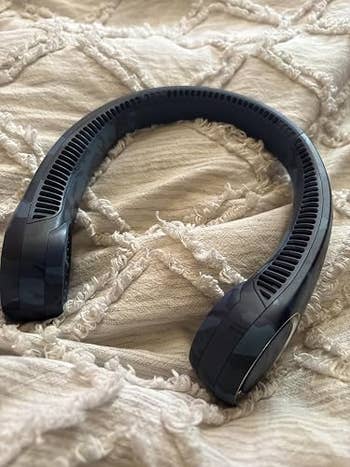A achromatic cervix instrumentality rests connected a textured blanket, showcasing its portable and hands-free plan for idiosyncratic cooling
