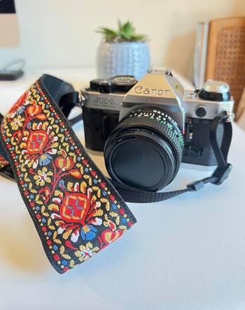 a woven vintage style embroidered camera strap in red, blue, white, and yellow colors on a camera 