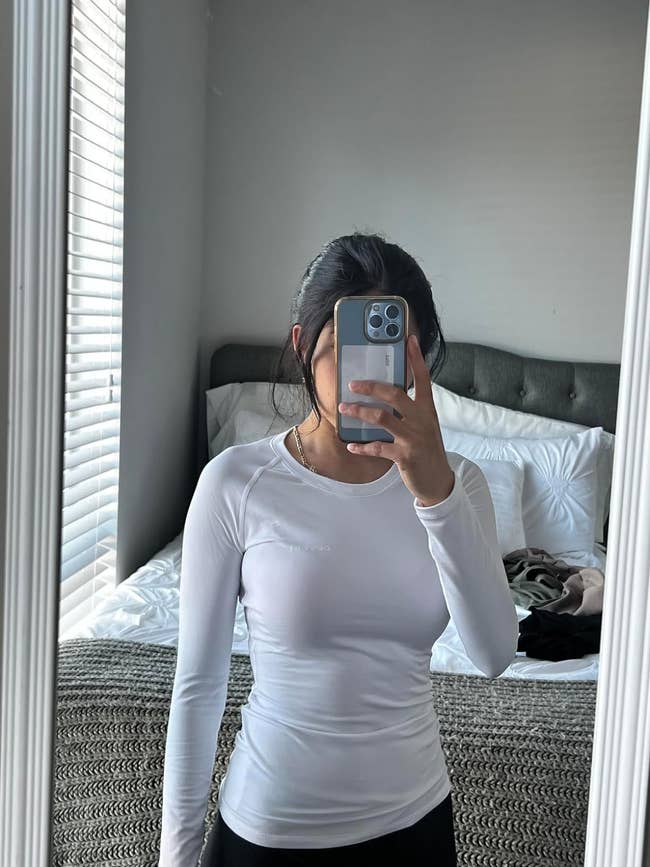Person in white top taking a selfie in mirror, phone covering face, casual style