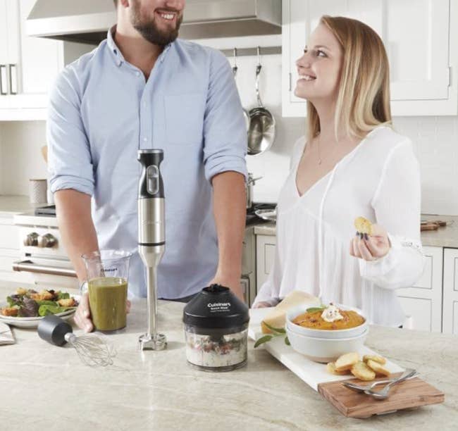 Two models standing in front of the hand mixer and various blended items