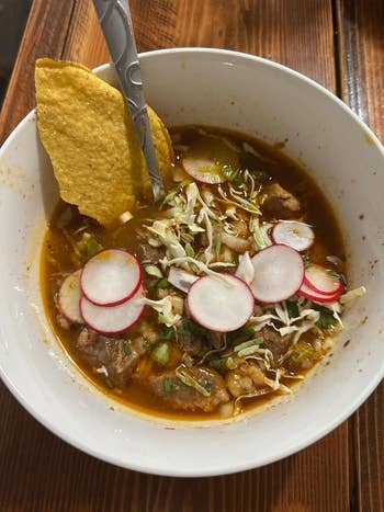 Bowl of hearty soup topped with sliced radishes, cabbage, and a tortilla chip, served with a spoon
