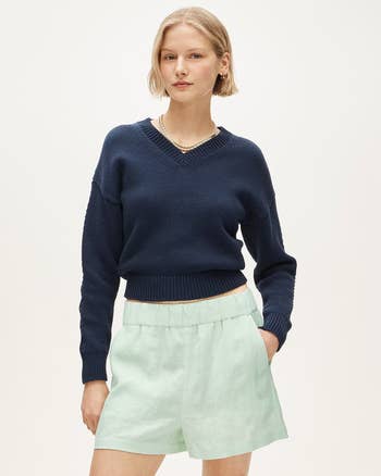 Person wearing a casual, long-sleeve sweater and high-waisted shorts, posing with hands successful pockets