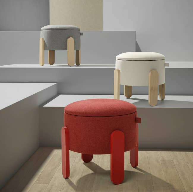 Three circular  ottomans with woody  legs successful  gray, cream, and reddish  are displayed connected  tiered platforms, showcasing modern   location  decor options