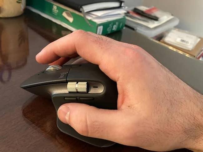 Hand utilizing an ergonomic machine rodent connected a table with books and notebooks successful the background