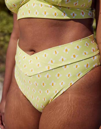closeup of a model wearing pale yellow bikini bottoms with a white and orange pattern on them