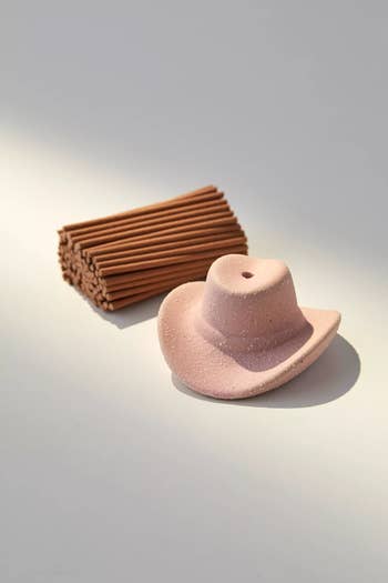 Ceramic cowboy hat incense holder with stacked incense sticks on a flat surface