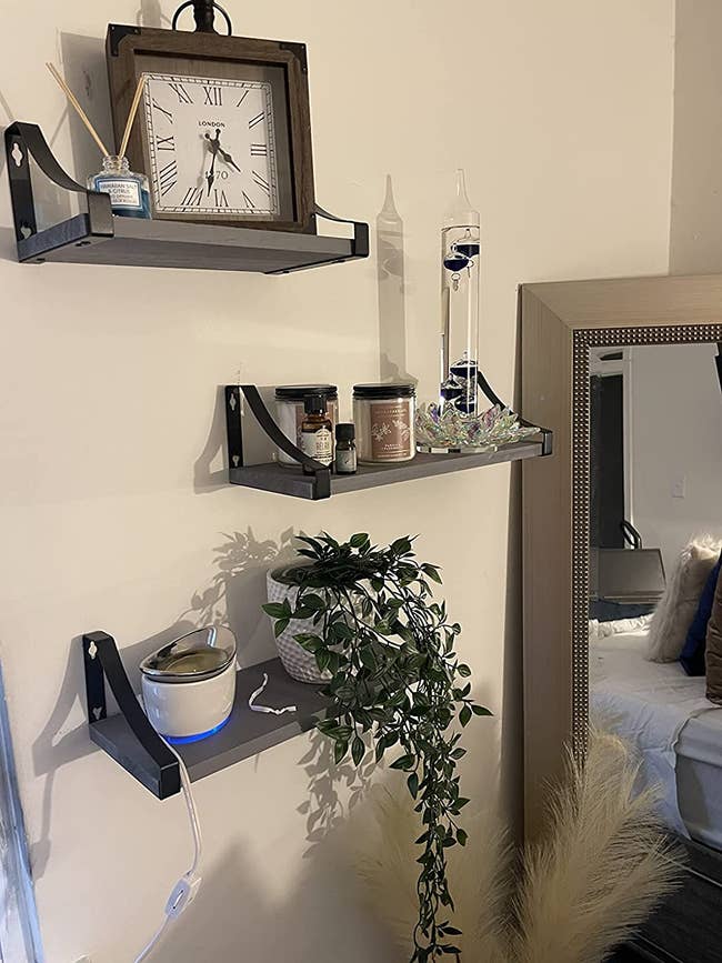 a reviewer's three grey shelves hanging from their wall with various decorations/plants/candles on them