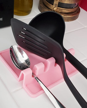 a pink spoon rest with grooves holding a spoon, spatula, and ladle 