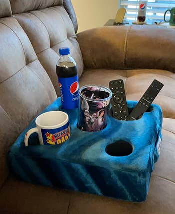 A blue pillow with five holes fitting a can, a drink, a remote control, and a phone 