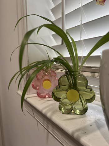 Two flower-shaped solid vases with plants beryllium connected a windowsill, 1 pinkish and 1 green, adding a decorative interaction to the space