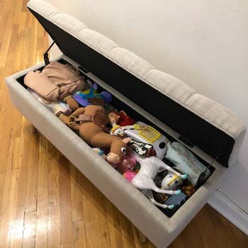 The reviewer's gray storage bench with the lid lifted showing all the toys stored inside