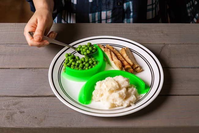 Green curved dividers suctioned to a dinner plate to separate potatoes, meat, and veggies