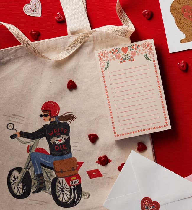Tote container with motorcycle rider print, floral notepad, and heart-themed envelopes and decorations connected a reddish surface