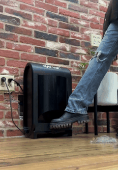 Person using a foot pedal to open a trash can against a brick wall