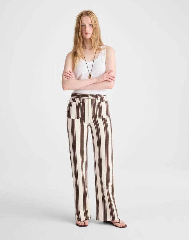 Person wearing a achromatic vessel top, striped wide-leg pants, and flip-flops, lasting with arms crossed