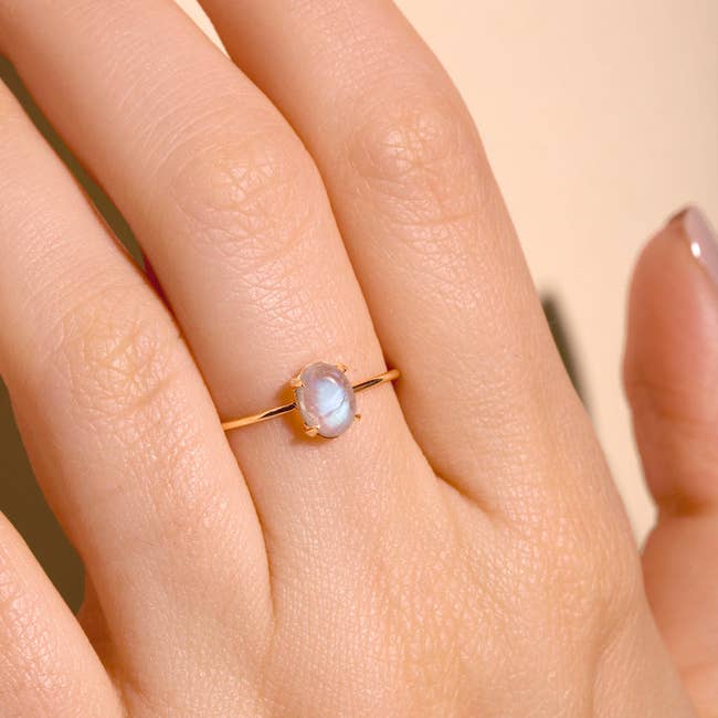 a model wearing the ring with a simple thin gold band and an opal center