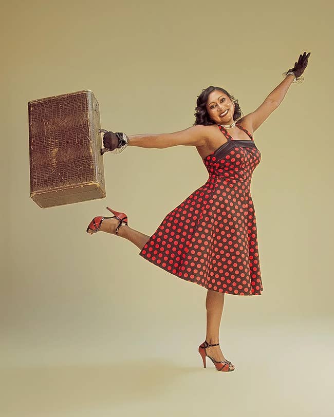 Person joyfully posing successful a vintage polka dot dress, holding a suitcase, with an look of excitement