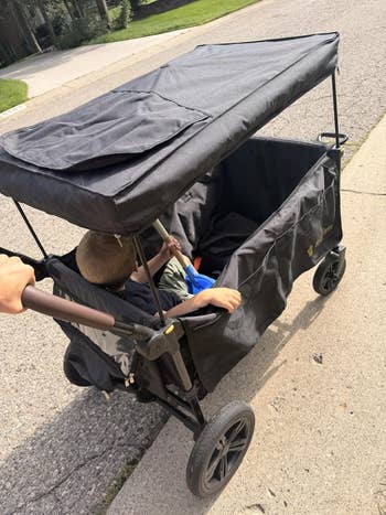 Child seated successful a spacious, covered stroller wagon being pushed extracurricular connected a sidewalk