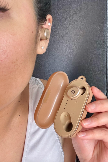 reviewer holding earbud case with one earbud in their ear