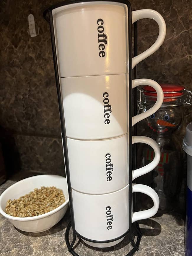 Four stacked white coffee canisters in a metal holder on a kitchen counter