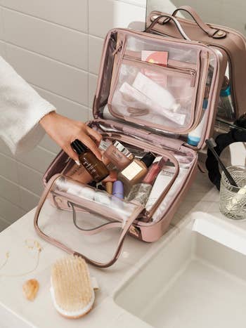 model taking makeup out of clear mauve toiletry bag
