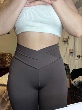 Woman wearing high-waisted leggings with a crossover waistband and a sleeveless ribbed top. Fashionable and comfy activewear style