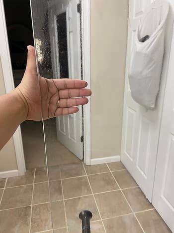 The same shower door with reviewer hand, but the door is completely clear and clean
