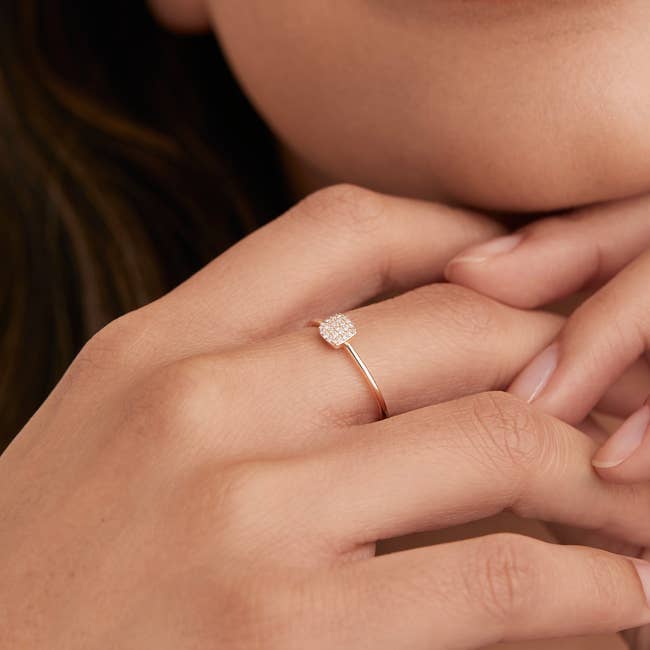 a model wearing the ring that has mini diamonds in a square shape with a thin gold band