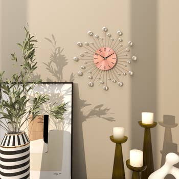 Modern living room with a sunburst wall clock, potted plant, framed artwork, and candle holders, creating a stylish, cozy atmosphere