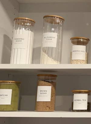 Clear labeled containers on shelves with various dry goods for organized pantry storage