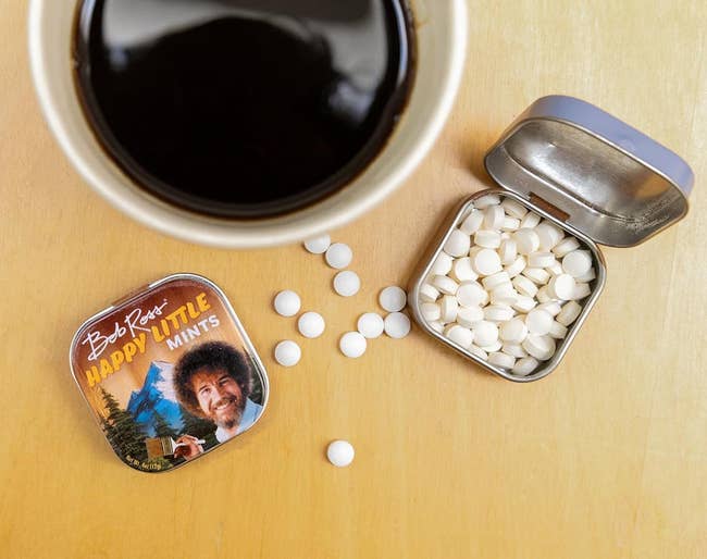 Open tin of Bob Ross-themed mints adjacent to a java cupful connected a table, with a fewer mints scattered extracurricular the tin