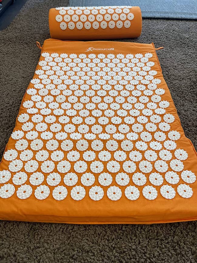 reviewer's orange acupressure mat and pillow on the floor