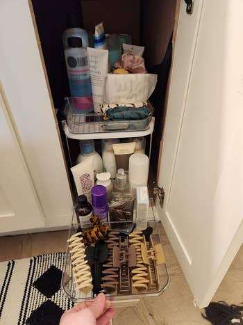 another reviewer pulling out the bottom drawer of their organizer to reveal hair supplies, which is stored in a cabinet