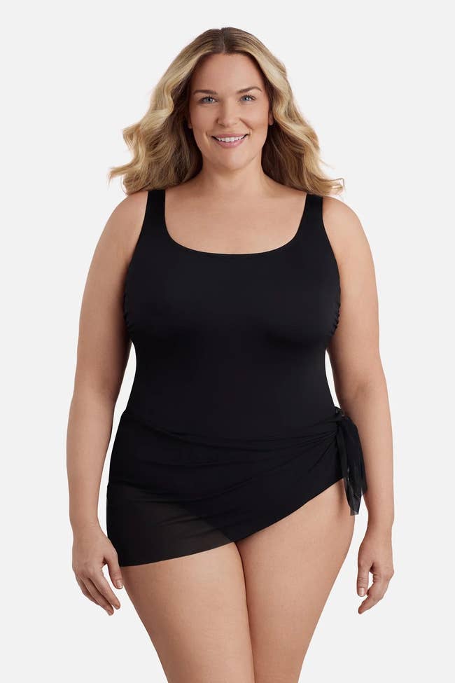 A person models a stylish black swimsuit with a sheer wrap detail, suitable for plus-size fashion shopping