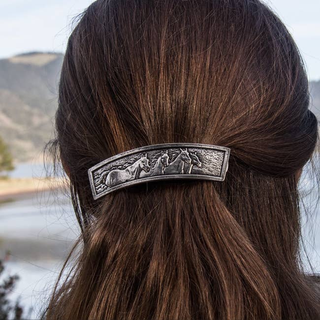Model with long hair wearing a decorative hair clip featuring a detailed horse design
