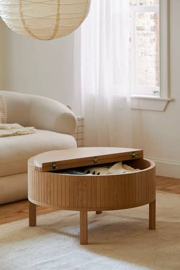 Round wooden coffee table with lift-top storage feature in a cozy living room setting