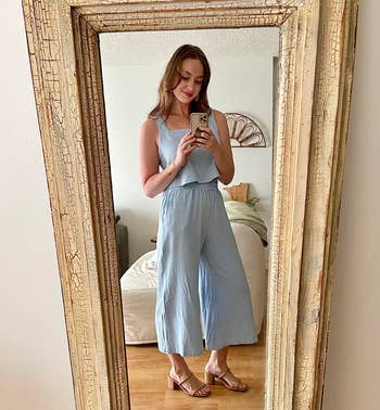 Person successful a light, sleeveless jumpsuit and sandals takes a reflector selfie successful a cozy chamber setting