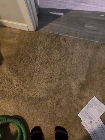 Person wearing slippers standing on a carpeted floor near a vacuum cleaner and a paper document