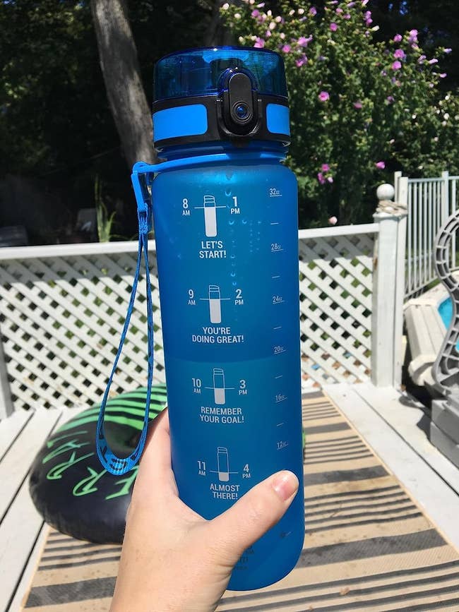 Reviewer holding blue water bottle with white time markings on them 