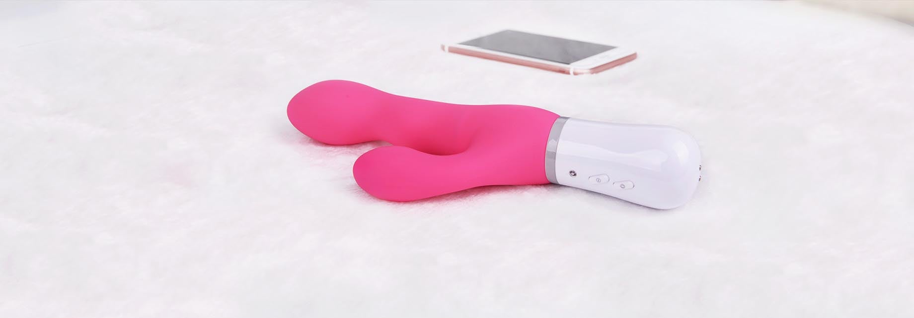 Pink rabbit vibrator next to cell phone on mattress