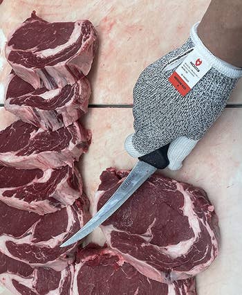 reviewer wearing one of the gloves while holding a knife near some sliced steaks