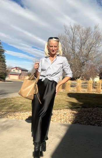 reviewer outdoors wearing a tied button-up shirt, agelong  skirt, and holding a stylish bag, suitable for casual shopping