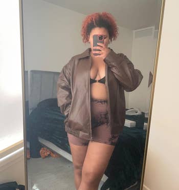 Person successful a brownish leather jacket, achromatic bra, and patterned shorts, taking a reflector selfie successful a bedroom