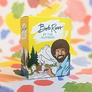 Bob Ross paint-by-numbers kit box featuring his illustration with mountains and trees in the background